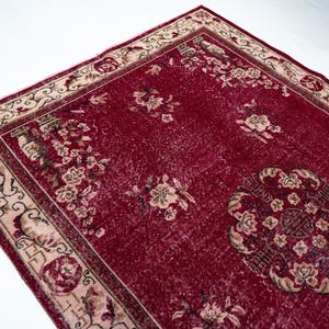 May include: A rectangular, distressed red rug with a floral pattern. The rug features a central medallion design and a cream-colored border with floral and geometric motifs. The rug's design includes beige and brown accents.