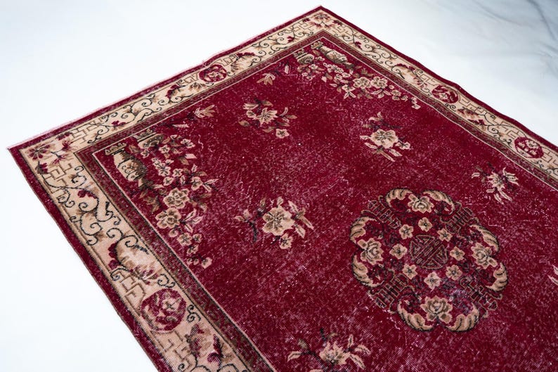 May include: A rectangular, distressed red rug with a floral pattern. The rug features a central medallion design and a cream-colored border with floral and geometric motifs. The rug's design includes beige and brown accents.