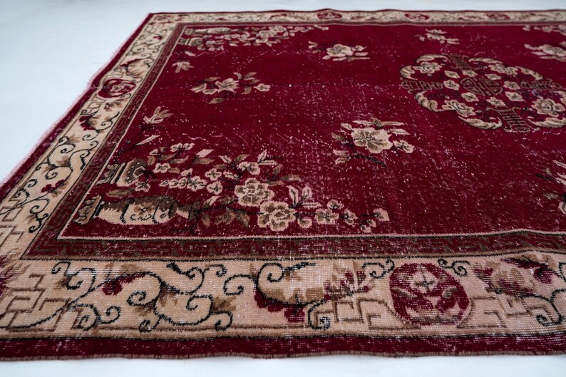 May include: A rectangular, vintage-style rug with a deep red field and a beige border. The rug features floral patterns in beige and brown, with a central medallion design. The border has intricate scrollwork and geometric elements.