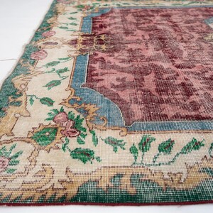 May include: An antique rug with a distressed, vintage appearance. The rug features a central maroon field with a floral pattern, framed by a cream border with green, blue, and gold accents. The rug's design includes floral and botanical motifs.