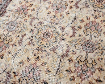 Può includere: Primo piano di un tappeto vintage con un intricato motivo floreale. Il tappeto presenta uno sfondo color crema con motivi floreali sbiaditi rossi, marroni e dorati. Il design ha un aspetto invecchiato e antico, suggerendo che si tratta di un tappeto tradizionale.