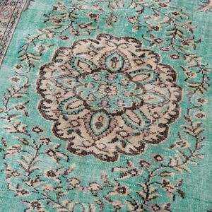 May include: A rectangular, distressed-look rug with a central medallion design. The rug features a teal background with a beige and brown floral pattern. The border has a similar design. This rug is suitable for living rooms and bedrooms.