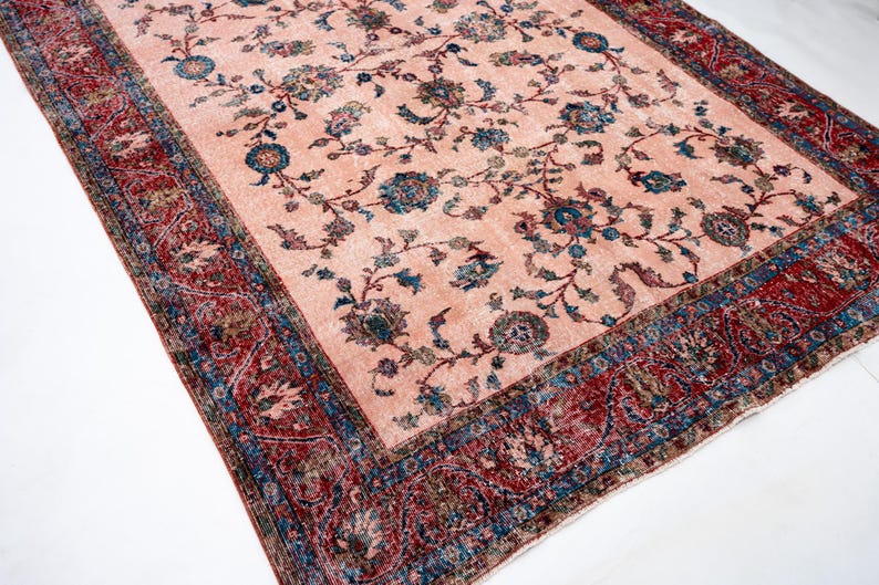 Pu&ograve; includere: Un tappeto rettangolare in stile vintage con un campo centrale color pesca. Presenta un motivo floreale in verde acqua e blu, con un bordo dettagliato rosso e blu. Il design suggerisce un'estetica tradizionale e antica, adatta all'arredamento.
