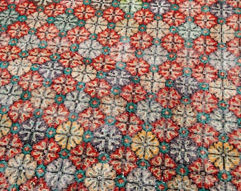 May include: Close-up of a patterned rug with a repeating floral design. The rug features a mix of colors, including red, teal, yellow, gray, and purple. The floral pattern is set against a neutral background.