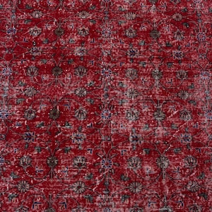 K&ouml;nnte beinhalten: Ein roter, abgenutzter Teppich mit einem komplizierten Blumenmuster. Der Teppich hat ein rotes Mittelfeld mit sich wiederholenden Blumenmotiven in Braun-, Blau- und Gr&uuml;nt&ouml;nen. Ein Rand mit Blumenmustern in Rosa und Blau umrahmt den Teppich.