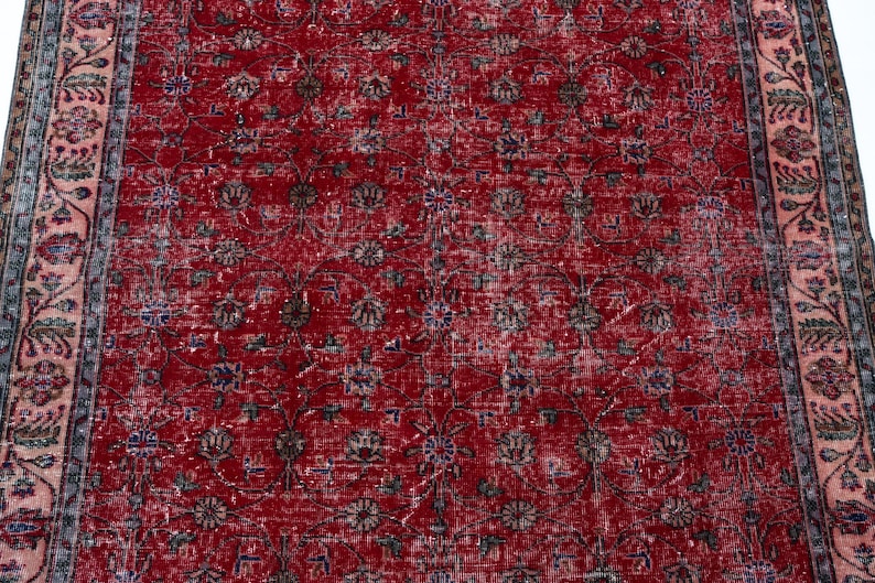 K&ouml;nnte beinhalten: Ein roter, abgenutzter Teppich mit einem komplizierten Blumenmuster. Der Teppich hat ein rotes Mittelfeld mit sich wiederholenden Blumenmotiven in Braun-, Blau- und Gr&uuml;nt&ouml;nen. Ein Rand mit Blumenmustern in Rosa und Blau umrahmt den Teppich.