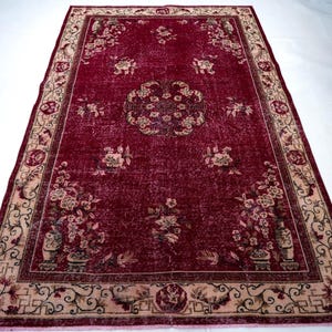 May include: A rectangular, vintage-style rug with a deep red field and a beige border. The rug features floral patterns and a central medallion design. The border has intricate scrollwork and floral motifs. The rug's design suggests a classic, antique aesthetic.