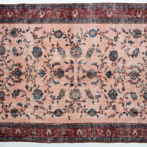 Pu&ograve; includere: Tappeto rettangolare con centro color pesca e motivo floreale in verde acqua e blu navy. Il bordo &egrave; rosso scuro con un design dettagliato. Il tappeto ha un aspetto vintage e usurato.