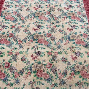 Pode incluir: Um tapete floral vintage com fundo creme e um padr&atilde;o de flores rosa, azuis e roxas. O tapete tem uma borda vermelha escura. Adequado para salas de estar e quartos. Mede aproximadamente 200 cm x 300 cm.
