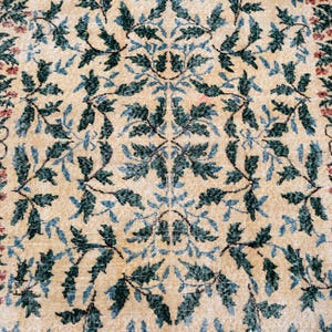 May include: Beige rug with a repeating pattern of green and blue leaves and red flowers. The rug has a distressed, vintage look, with a faded appearance. The floral design is symmetrical, creating a classic, elegant aesthetic.