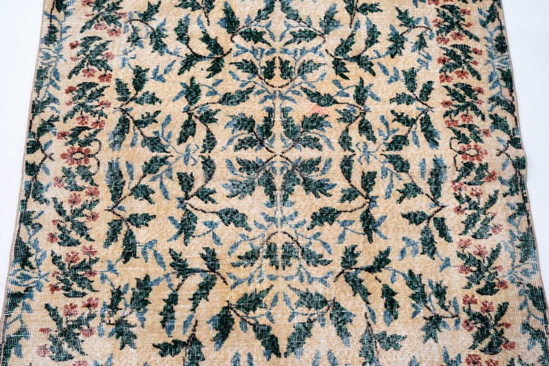 May include: Beige rug with a repeating pattern of green and blue leaves and red flowers. The rug has a distressed, vintage look, with a faded appearance. The floral design is symmetrical, creating a classic, elegant aesthetic.