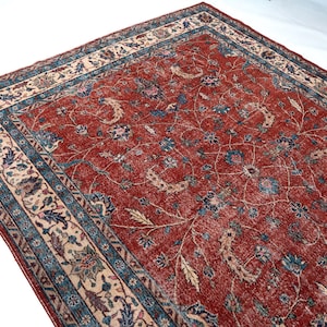 May include: A rectangular, distressed red rug with an intricate floral pattern. The rug features a cream-colored border with blue and beige accents. The central design showcases blue and cream-colored floral motifs.