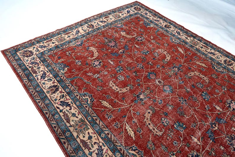 May include: A rectangular, distressed red rug with an intricate floral pattern. The rug features a cream-colored border with blue and beige accents. The central design showcases blue and cream-colored floral motifs.