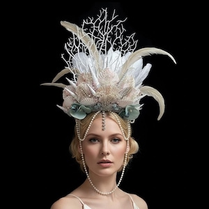Può includere: Copricapo dettagliato a tema sirena. La corona presenta coralli bianchi, piume e conchiglie, con accenti di rosa pallido e verde acqua. Un copricapo e una collana con catena di perle e oro completano il look.