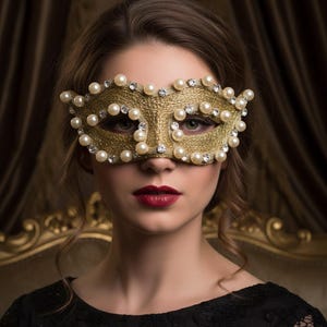 May include: Gold masquerade mask adorned with pearls and rhinestones. The mask is a metallic gold color and covers the eyes and upper face. The mask is decorated with numerous faux pearls and small rhinestones. The person in the image is wearing a black dress and red lipstick.