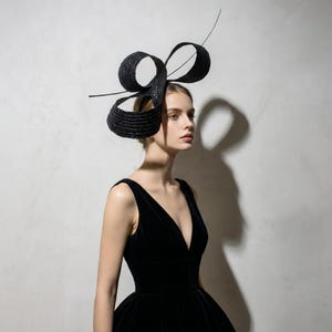 Könnte beinhalten: Ein schwarzes Kopfstück mit einem großen, geschlungenen Design und einem dünnen, gebogenen Akzent. Das Kopfstück wird mit einem schwarzen Kleid getragen. Das Kopfstück ist ein formelles Accessoire.