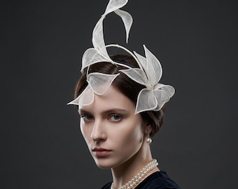 Puede incluir: Tocado blanco con forma floral, con un diseño de tejido abierto y delicado. El tocado se lleva en la cabeza y se acentúa con un collar y pendientes de perlas. El fondo es gris oscuro liso.