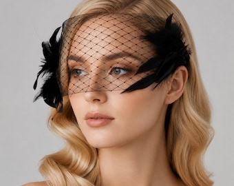 Puede incluir: Un velo tipo jaula negro con una red de patrón de diamante fino que cubre la parte superior del rostro. El accesorio está adornado con plumas negras unidas a ambos lados, creando un aspecto estructurado que se extiende hacia las sienes.