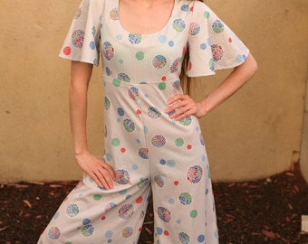 May include: A white jumpsuit with a blue, green, and red polka dot pattern. The jumpsuit has a scoop neck and short sleeves. The sleeves have a bell shape.