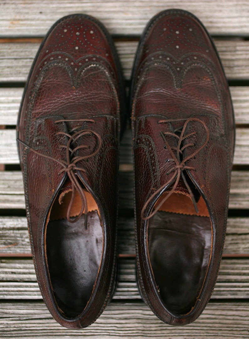 May include: A pair of brown leather shoes with wingtip detailing and laces. The shoes have a textured leather upper and a smooth leather sole.
