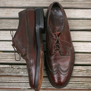 May include: A pair of brown leather lace-up shoes with wingtip detailing. The shoes have a textured leather upper and a polished finish.