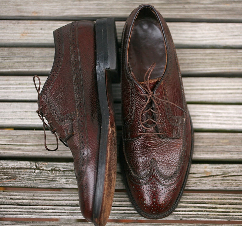 May include: A pair of brown leather lace-up shoes with wingtip detailing. The shoes have a textured leather upper and a polished finish.