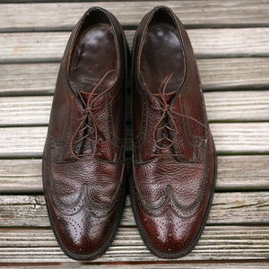 May include: A pair of brown leather lace-up shoes with wingtip detailing. The shoes have a textured leather upper and a polished finish.