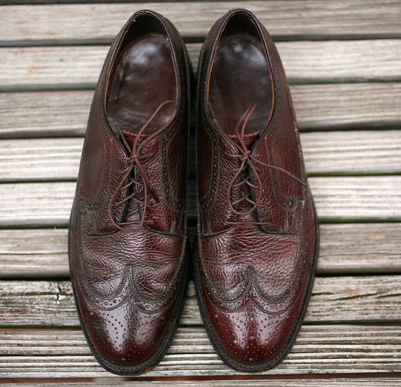 May include: A pair of brown leather lace-up shoes with wingtip detailing. The shoes have a textured leather upper and a polished finish.
