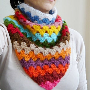 Peut inclure: Un col écharpe crocheté à la main, aux couleurs vives. L'écharpe présente une variété de couleurs, notamment rose, orange, violet, marron, jaune, bleu, vert et blanc. Le col est de forme triangulaire et semble être fait de fil doux.