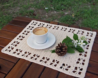 Peut inclure: Un napperon en crochet blanc avec une tasse de café et une pomme de pin sur une table en bois.