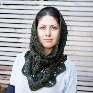 May include: A dark green crocheted hood and scarf combination. The hood frames the face, and the scarf portion has a scalloped edge with openwork details. The item is worn over a light-colored sweater.