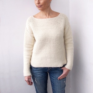 Peut inclure: Un pull en crochet blanc avec un col bateau et des manches longues. Le pull est réalisé avec un point texturé et a une coupe ample.