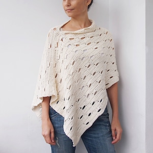 May include: A white crocheted poncho with a loose, open-weave design. The poncho has a high neckline and a slightly asymmetrical hemline.