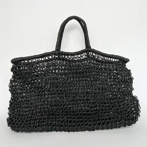 Könnte beinhalten: Eine schwarze gewebte Tragetasche mit zwei Griffen. Die Tasche hat eine rechteckige Form mit einer breiten Öffnung und einem strukturierten, offen gewebten Design. Die Griffe sind dick und robust, geeignet zum Tragen verschiedener Gegenstände.