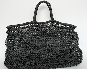 May include: A black woven tote bag with two handles. The bag has a rectangular shape with a wide opening and a textured, open weave design. The handles are thick and sturdy, suitable for carrying various items.