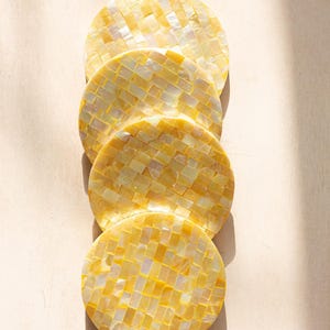 May include: Four circular coasters with a mosaic pattern in shades of yellow and white. The coasters are arranged vertically, with a light background and shadows.