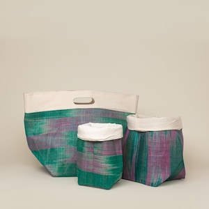 May include: Set of three fabric storage containers. The containers have a woven green and purple pattern with a cream-colored top. The largest container has a handle. The containers are designed for home organization.