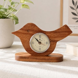May include: A wooden bird-shaped desk clock with a round clock face. The clock face has Roman numerals and black hands. The clock is made of light brown wood and sits on a matching base. The clock is a decorative item.