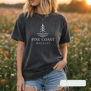 May include: A dark gray t-shirt with the text "PINE COAST MOCKUPS" and a tree graphic. The shirt is paired with denim shorts. The image is set in a field of flowers.