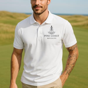 May include: A white polo shirt with short sleeves and a collared neckline. The shirt features a black graphic of a tree and waves, with the text "PINE COAST MOCKUPS" below. The shirt is worn on a person standing on a green field.