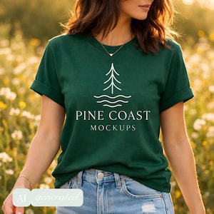 May include: A dark green short-sleeve t-shirt featuring a white graphic of a stylized pine tree above wavy lines. The text PINE COAST MOCKUPS is printed in white below the graphic. The shirt has a crew neckline and is paired with blue denim jeans.