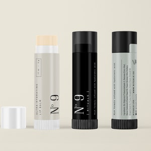 May include: Three cylindrical lip balm tubes, one light beige with a white cap, one black, and one light gray with a black cap. The tubes feature the text No 9, Ultra-Hydrating Lip Balm, and Rituals, with a net weight of .17 oz and 5 g listed.