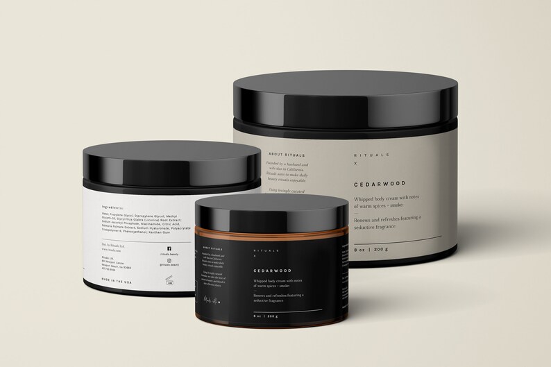 May include: Three black-lidded jars of body cream are displayed. The jars vary in size and have labels with text. The largest jar has a beige label with the text "CEDARWOOD". The smallest jar has a black label with the same text.