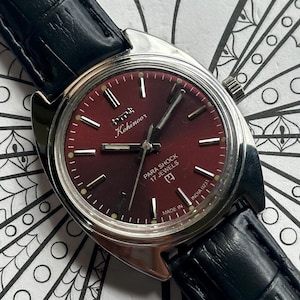 May include: A vintage Kohinoor wristwatch with a burgundy dial and silver case. The watch has a black leather strap and the text "PARA SHOCK 17 JEWELS" on the dial. The watch is marked "MADE IN INDIA".