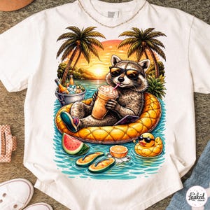 Peut inclure: T-shirt blanc avec un raton laveur de dessin animé portant des lunettes de soleil, se relaxant sur un flotteur ananas, buvant une boisson. Le motif comprend des palmiers, un coucher de soleil et un canard en caoutchouc. Le t-shirt porte le texte "Laaked Design".