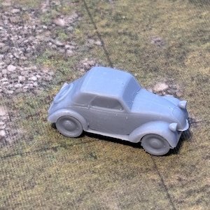 May include: A small, light gray toy car with a convertible top. The miniature vehicle has rounded fenders, headlights, and a detailed body. The car is set against a backdrop of a green and brown surface.