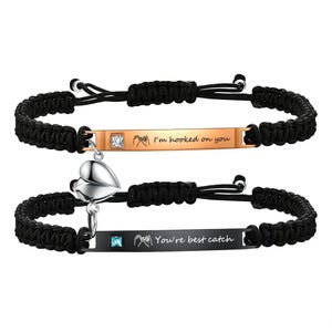 May include: Two matching black braided bracelets. One has a gold-colored bar with the text "I'm hooked on you" and a small square gem. The other has a black bar with "You're best catch" and a heart charm.