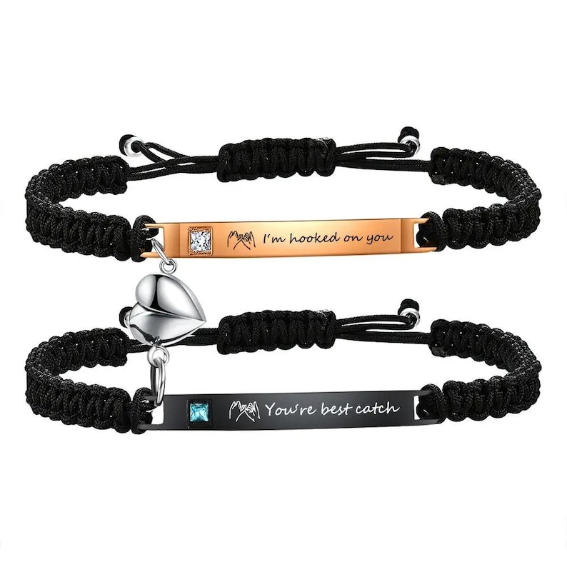 May include: Two matching black braided bracelets. One has a gold-colored bar with the text "I'm hooked on you" and a small square gem. The other has a black bar with "You're best catch" and a heart charm.