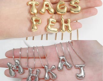 May include: Gold and silver-toned initial necklaces. The gold necklaces spell out "TAGS PEH". The silver necklaces spell out "M H K A J". Each necklace features a bubble letter pendant on a delicate chain.