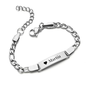Peut inclure: Un bracelet argenté avec un motif de chaîne. Il comporte une plaque rectangulaire gravée du nom "Martín" et d'un petit symbole de cœur noir. Le bracelet est doté d'une fermeture à fermoir et d'une chaîne réglable.